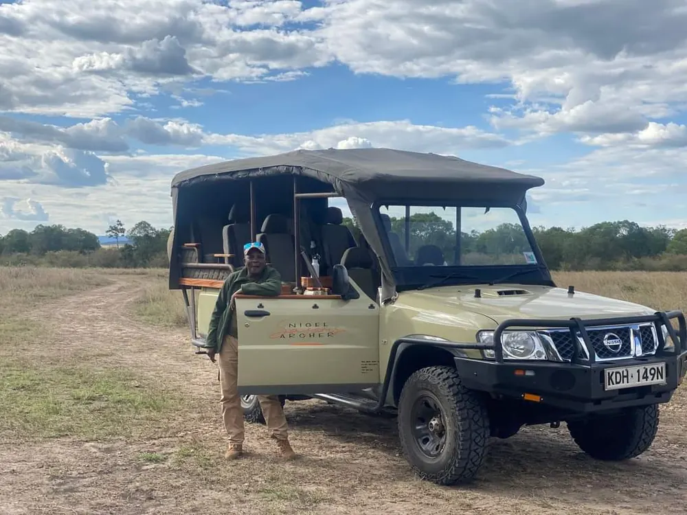 A senior guide standing beside the open safari Land Cruiser on the plains