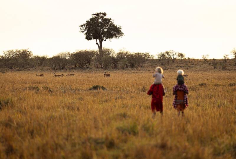 Two children in red shukas walking out across the Mara grass