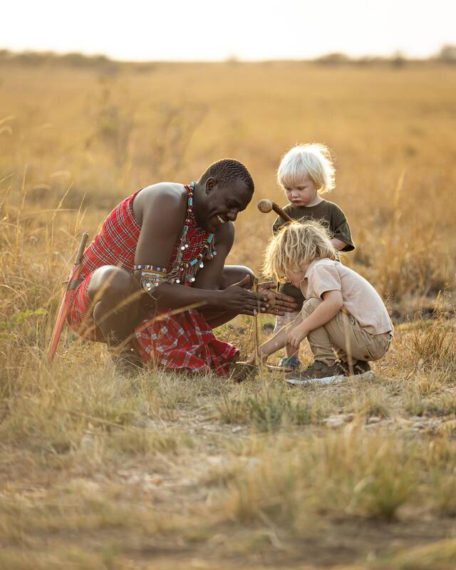 A Maasai guide showing two young children something in the grass