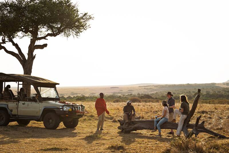 Guests and guides gathered round a fallen log under an acacia