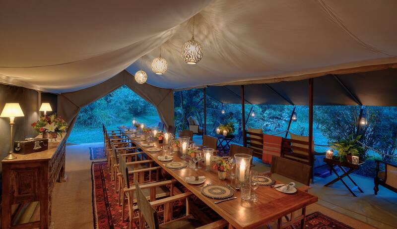 The long mess table set for dinner at dusk, under hanging lanterns